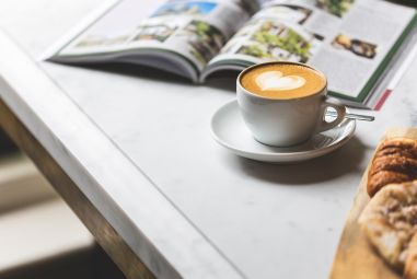 Cappuccino und Zeitschrift auf Tisch